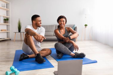 Siyah çift spor salonundan sonra dinleniyor, çevrimiçi spor videoları izliyor, ekrana işaret ediyor, egzersizleri tartışıyor.