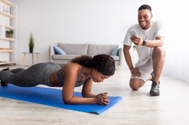 Genç siyah çift evde takım olarak çalışıyor, formda bayan dirsek kalasında duruyor, erkek arkadaşı akıllı telefondan saati not ediyor.