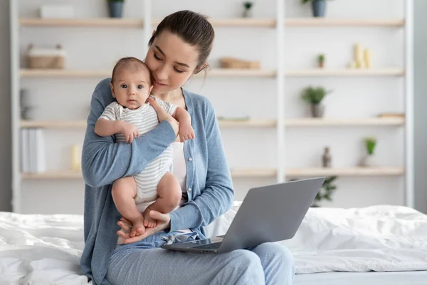 Porträtt av ung lycklig mor hålla nyfödda barn och använda bärbar dator — Stockfoto