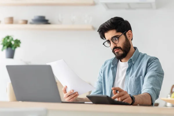 Une vie moderne coûteuse. Homme arabe déçu calculant les impôts ou le budget de planification tout en étant assis à la table de cuisine — Photo