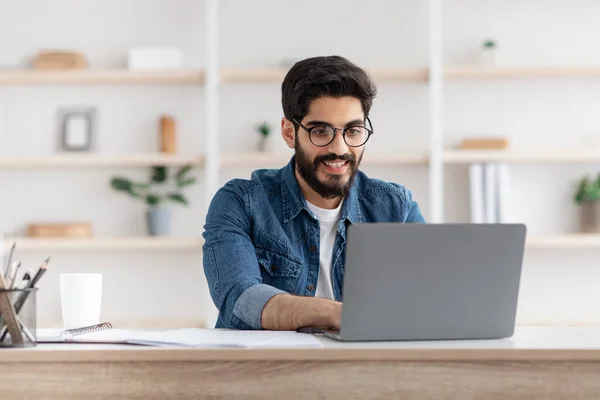 Freiberufliche Tätigkeit. Glücklicher arabischer Mann, der zu Hause im Büro am Computer arbeitet, am Arbeitsplatz mit Laptop sitzt, leerer Raum — Stockfoto