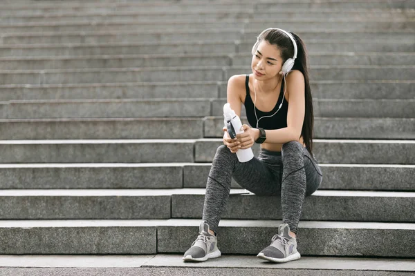 Después del ejercicio exitoso. Joven mujer coreana descansando en los pasos al aire libre, escuchando música — Foto de Stock