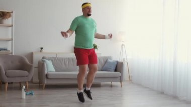 Şişman adam ip atlayıp atlıyor, iç mekanda spor antrenmanı yapıyor, çekim takibi yapıyor.