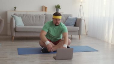Nilüfer pozisyonunda oturan şişman adam dizüstü bilgisayara ve meditasyona karşı evde yerde nefes egzersizi yapıyor.