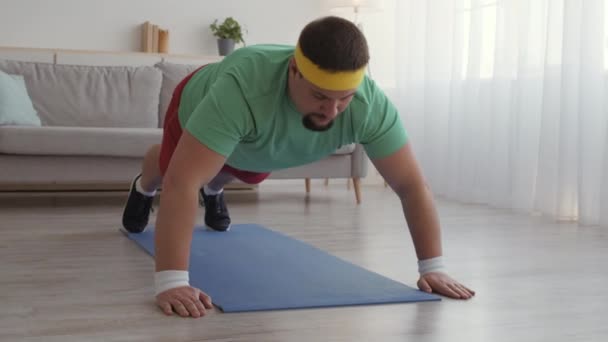 Tracking shot de hombre con sobrepeso practicando flexiones en casa, apenas haciendo ejercicio en el suelo, cámara lenta — Vídeos de Stock