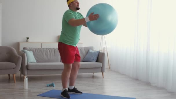 Grappige overgewicht man oefenen diepe kraakpanden met fitball thuis, tracking shot, slow motion — Stockvideo