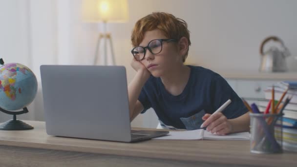 Saaie online onderwijs. Moe roodharige jongen die thuis webinar of videoles kijkt, naar laptop kijkt en zich moe voelt — Stockvideo