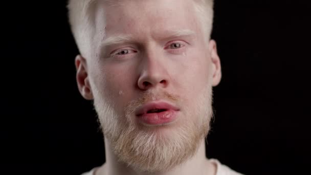Человек-альбинос плачет, глядя на камеру на черном фоне — стоковое видео