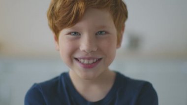 Yüzünde çilli, gülümseyen ve kameraya poz veren mutlu, sevimli, kızıl saçlı çocuğun portresini yakından çek.