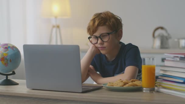 Söt rödhårig liten pojke sitter mot laptop, videokonferens med lärare, gäspar och sträcker ut sin kropp — Stockvideo