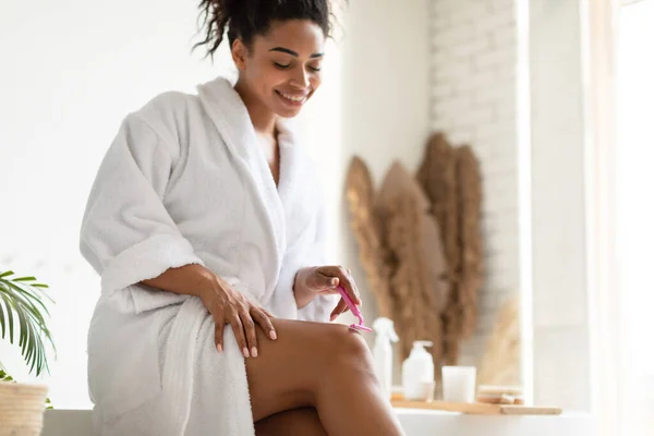 Ευτυχισμένη μαύρη γυναίκα κάνει αποτρίχωση ξύρισμα πόδια στο σύγχρονο μπάνιο — Φωτογραφία Αρχείου