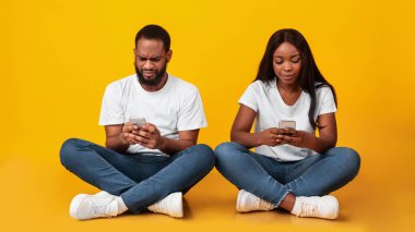 Stüdyoda yerde oturan akıllı telefon kullanan siyah bir çift.