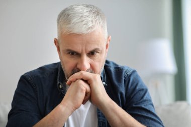 Evdeki kanepede oturan düşünceli kıdemli adam.