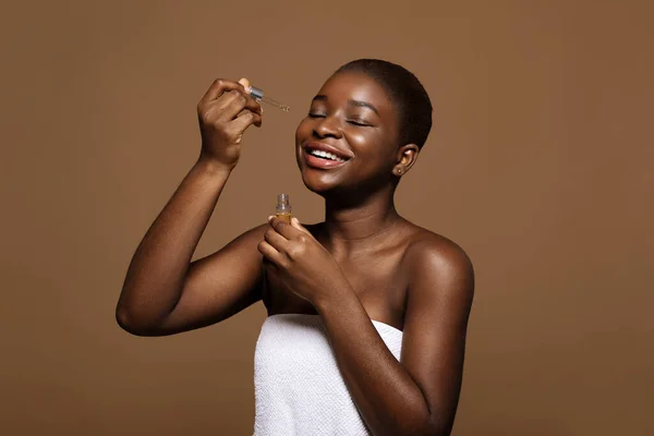 Routine della cura della pelle. felice bella nero femmina applicazione idratante viso siero dopo bagno — Foto Stock