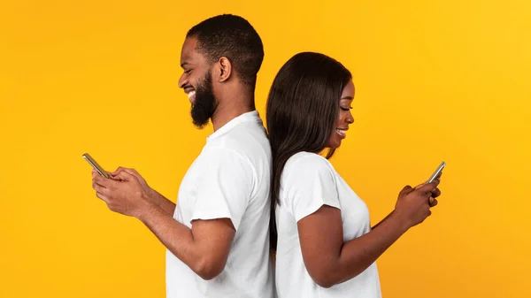 Pasangan Afrika Amerika menggunakan smartphone, dinding studio kuning — Stok Foto