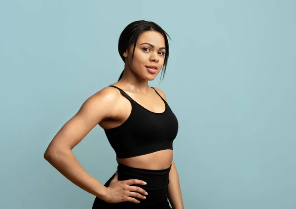 En hälsosam livsstil. Självsäker afrikansk amerikansk dam i sportkläder poserar och tittar på kameran på blå bakgrund — Stockfoto