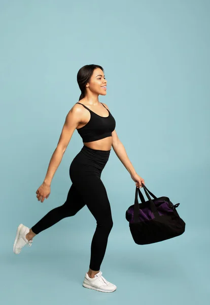 健康的なライフスタイルのコンセプト。青い背景の上にジムに走るフィットネスバッグを持つスポーティアフリカ系アメリカ人女性 — ストック写真