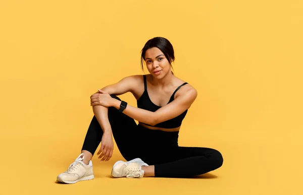 Bienestar y entrenamiento. Feliz mujer afroamericana deportiva sentada en el suelo en el fondo amarillo del estudio —  Fotos de Stock