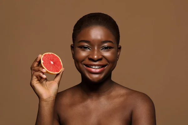 Concetto organico di cura della pelle. Ritratto di bella signora nera sorridente che tiene metà pompelmo — Foto Stock