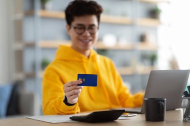 Evde kredi kartı gösteren gülümseyen Asyalı adam.