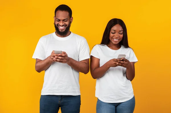 Casal preto usando smartphones, de pé no estúdio — Fotografia de Stock