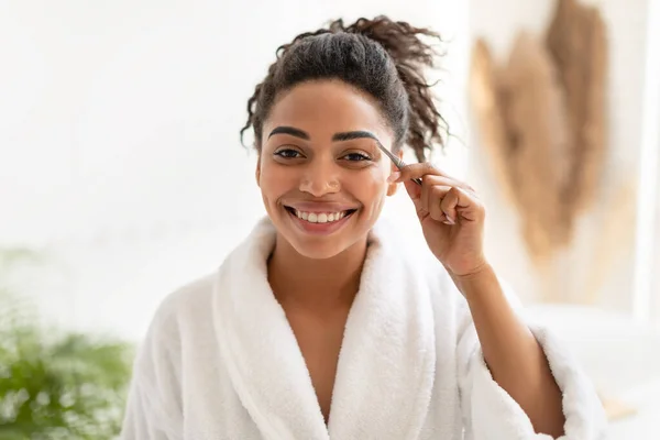 Africký americký žena styl škubání obočí s pinzetou v koupelně — Stock fotografie