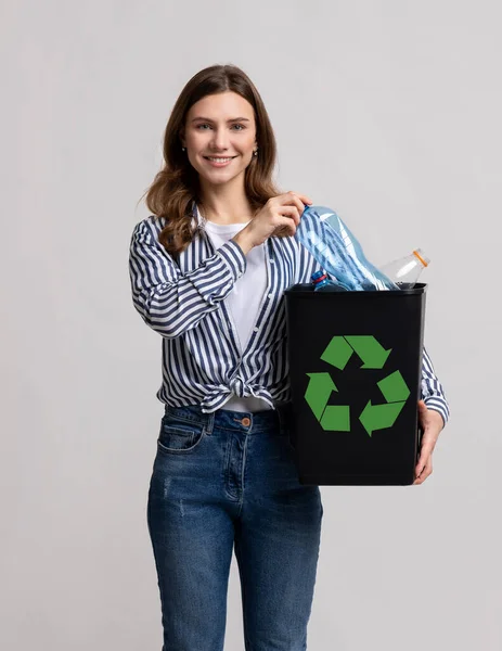 Reutilização Plástica. Senhora Millennial positiva carregando recipiente preto enchido com garrafas vazias — Fotografia de Stock