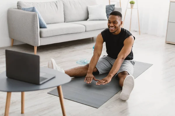 Μαύρος κάνει τεντώνοντας άσκηση γυμναστικής στο φορητό υπολογιστή στο σπίτι — Φωτογραφία Αρχείου