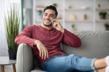 Kanepeye yaslanıp telefonda konuşan mutlu bir orta doğulu.