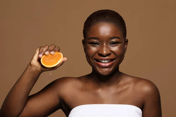 Vitamina C para a pele. alegre bela mulher negra espremendo laranja fruta metade — Fotografia de Stock