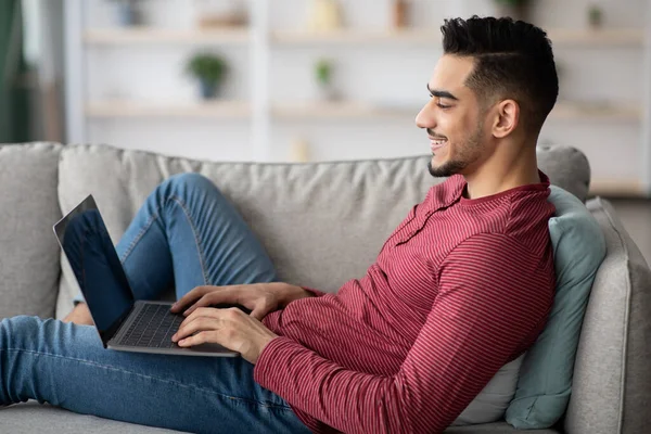 Relajado chico árabe utilizando el ordenador portátil con pantalla en blanco, interior del hogar — Foto de Stock
