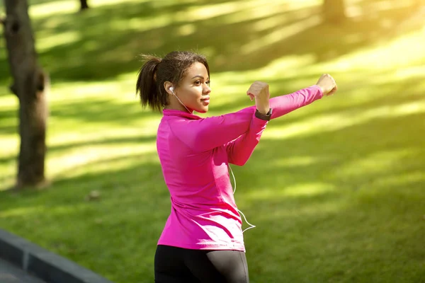 Весела атлетична чорна леді розтягує руки, тренування в парку — стокове фото