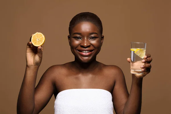 Bere sano. Sorridente signora nera in possesso di un bicchiere d'acqua e limone a metà — Foto Stock