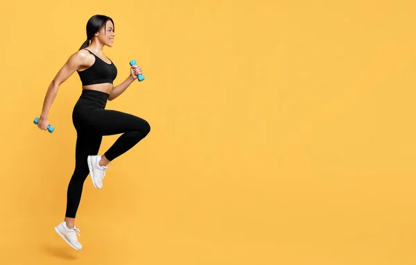 Conceito de exercícios esportivos. Jovem afro-americana exercitando com dois halteres, fundo de estúdio amarelo — Fotografia de Stock