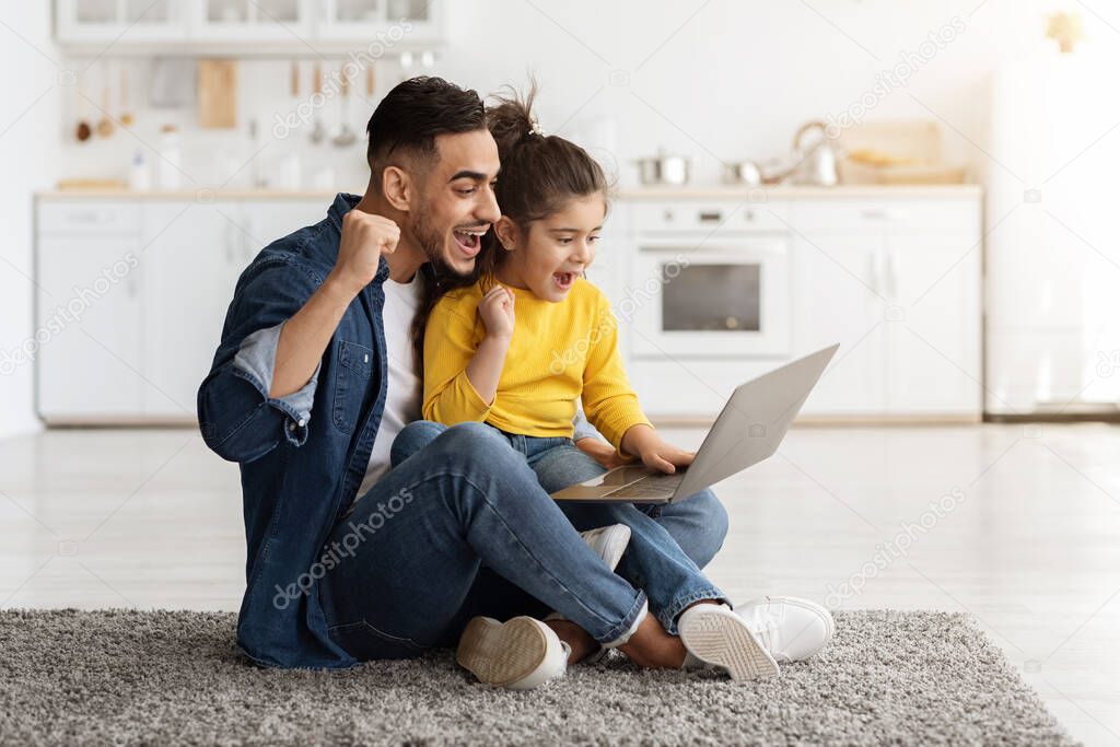 Young arab dad and little daughter celebrating success with laptop at home