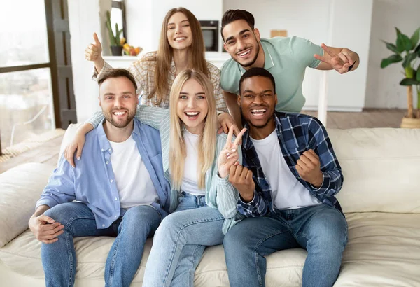 Retrato de amigos multirraciais felizes posando para foto, olhando para a câmera e sorrindo, sentado no sofá em casa — Fotografia de Stock