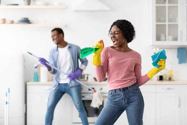 Joyful zwarte dame met behulp van spray als microfoon, zingen tijdens het schoonmaken — Stockfoto