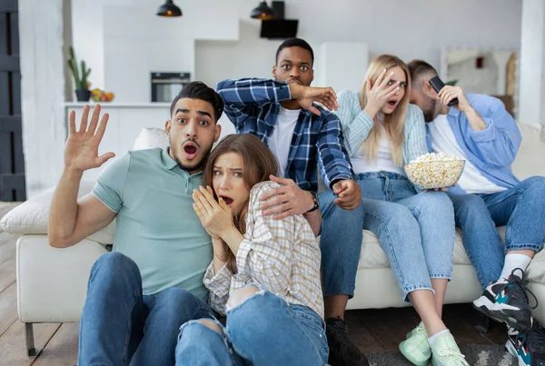 Verängstigte Millennial-Freunde sehen gruselige Filme oder Thriller, halten Popcorn in der Hand und bedecken zu Hause entsetzt ihre Gesichter. — Stockfoto