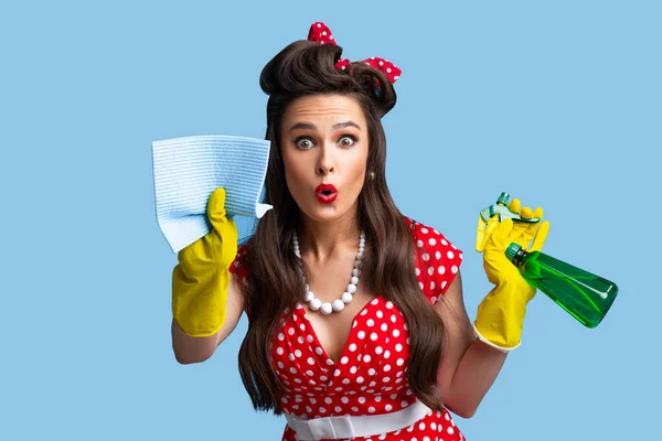 Überraschte Pinup-Dame in Retro-Kleidung Reinigungssieb mit Lappen, mit Sprühwaschmittel auf blauem Studiohintergrund — Stockfoto