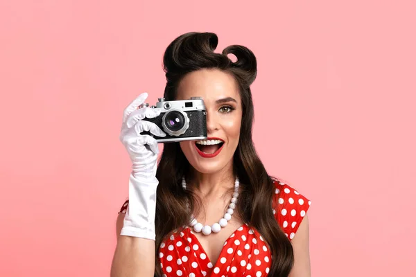 Porträtt av unga pinup kvinna med retro kamera tar bilder över rosa studio bakgrund — Stockfoto