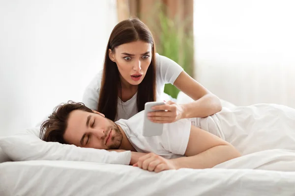 Шокированная девушка читает сообщения об измене мужей телефон в спальне — стоковое фото