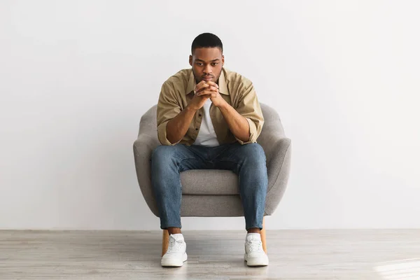 Reflexivo africano hombre pensamiento sentado en silla sobre gris fondo — Foto de Stock