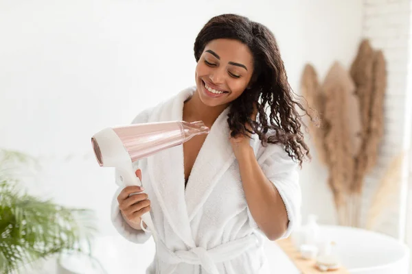 Gelukkig zwart dame drogen golvend haar met Haardroger in de badkamer — Stockfoto