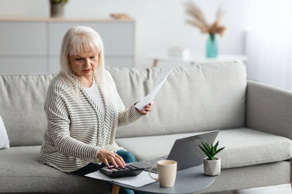 Elinde kağıt okuma raporu tutan bir kadın evde dizüstü bilgisayarla çalışıyor.