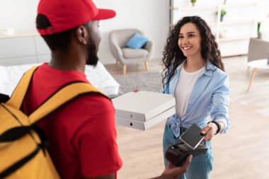 Siyah teslimatçı elinde pizza kutusu ve terminali tutuyor.