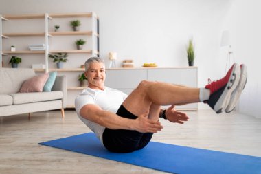 Mutlu kıdemli adam karın egzersizi yapıyor, vücut kaslarını çalıştırıyor, oturma odasında spor yapıyor.