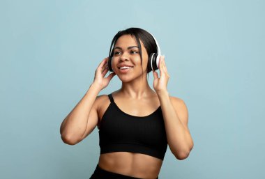 Müzikle çalış. Mutlu siyah kadın COVID-19 salgını sırasında mavi stüdyo arka planında ses egzersizi yapıyor.