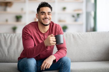 Kanepede oturup çay içen neşeli Arap adam.