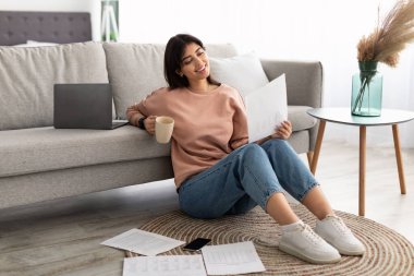 Elinde gazete okuyup evde kahve içen bir kadın.