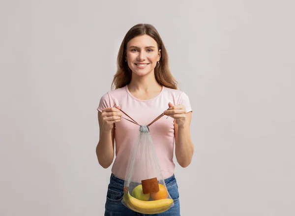 Jeune femme souriante portant un sac à ficelle en filet lavable avec des fruits biologiques — Photo